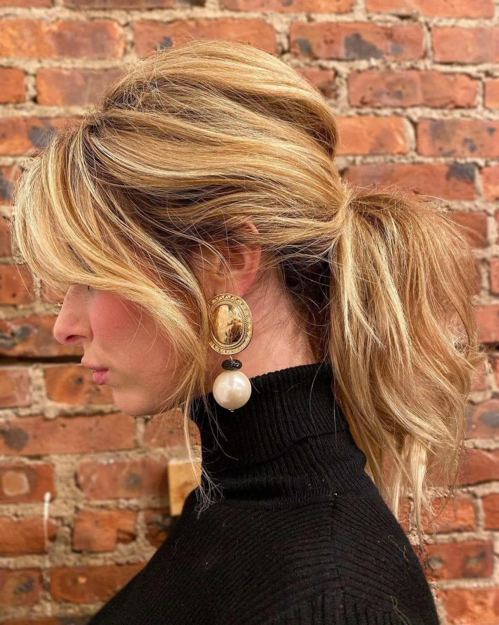 Elegant twisted low ponytail in golden caramel hues, paired with flattering curtain bangs.