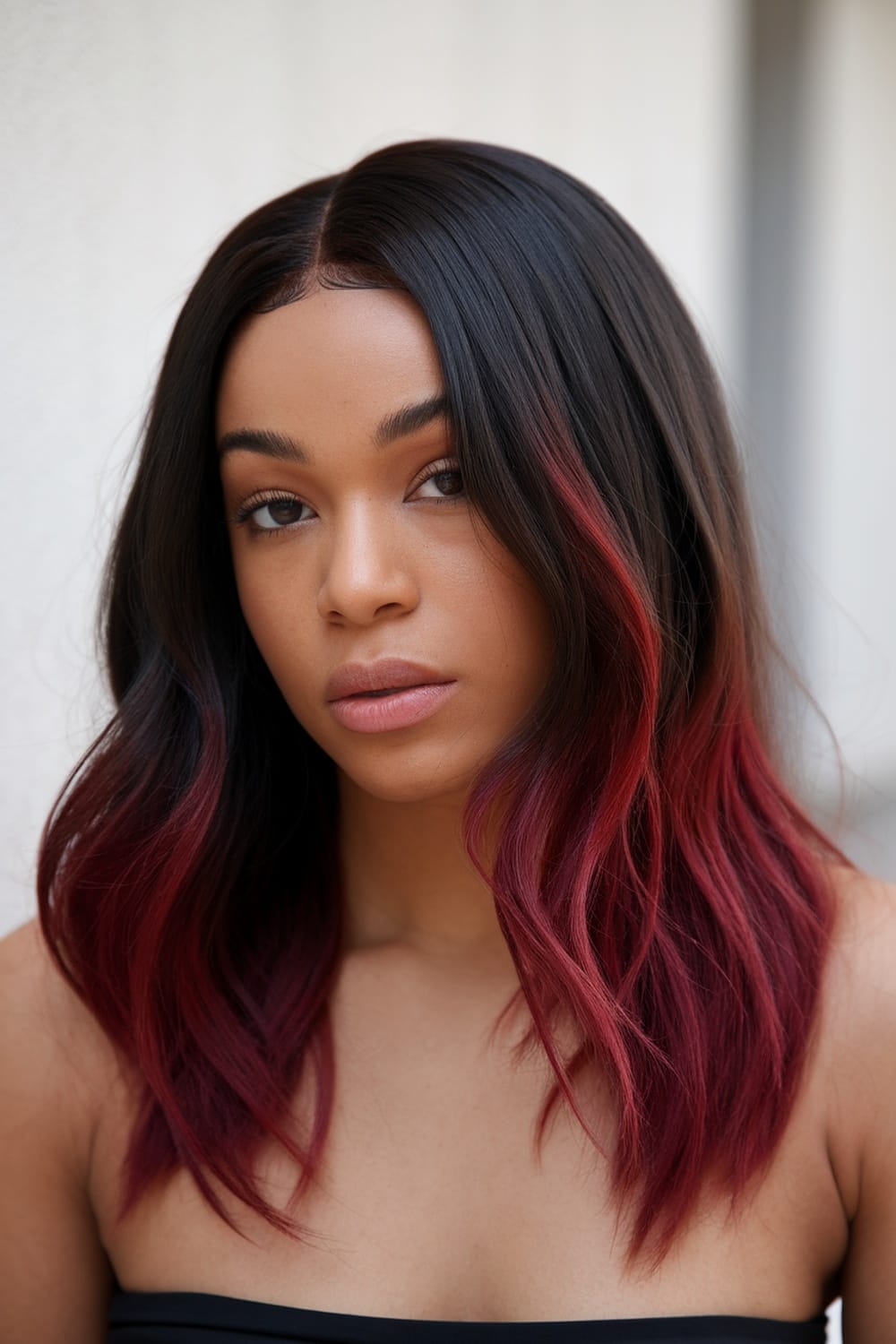 A woman with burgundy ombre hair, featuring dark roots and soft waves.