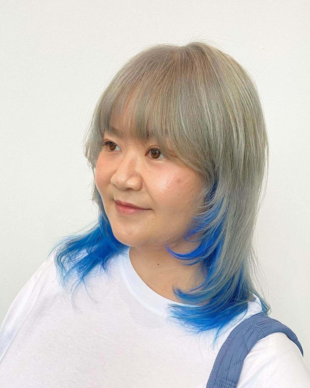 Playful hairstyle with straight fringe, ash and blue tones, and soft waves at tips.