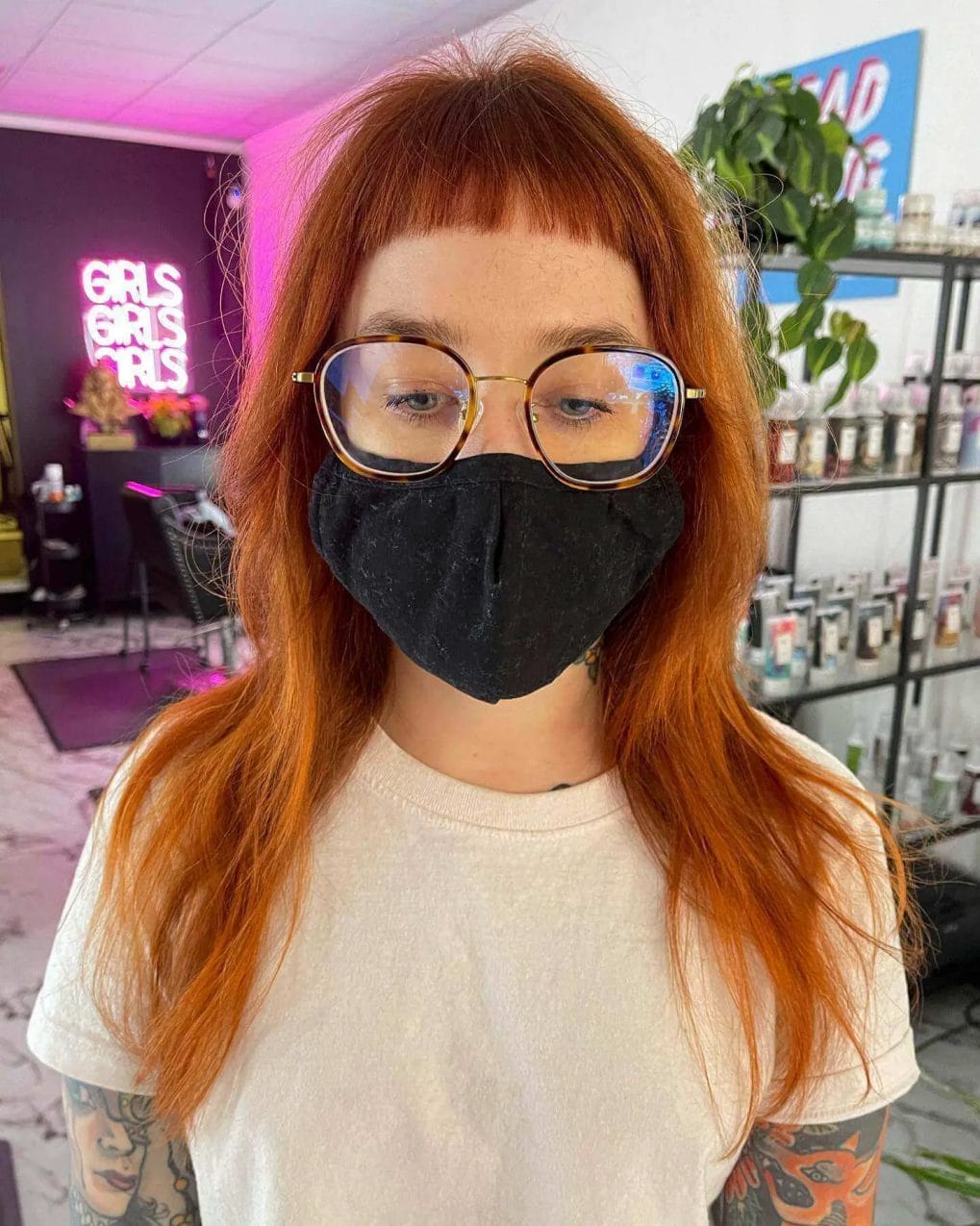 Shoulder-length fiery copper hair with straight fringe and bold glasses frames.