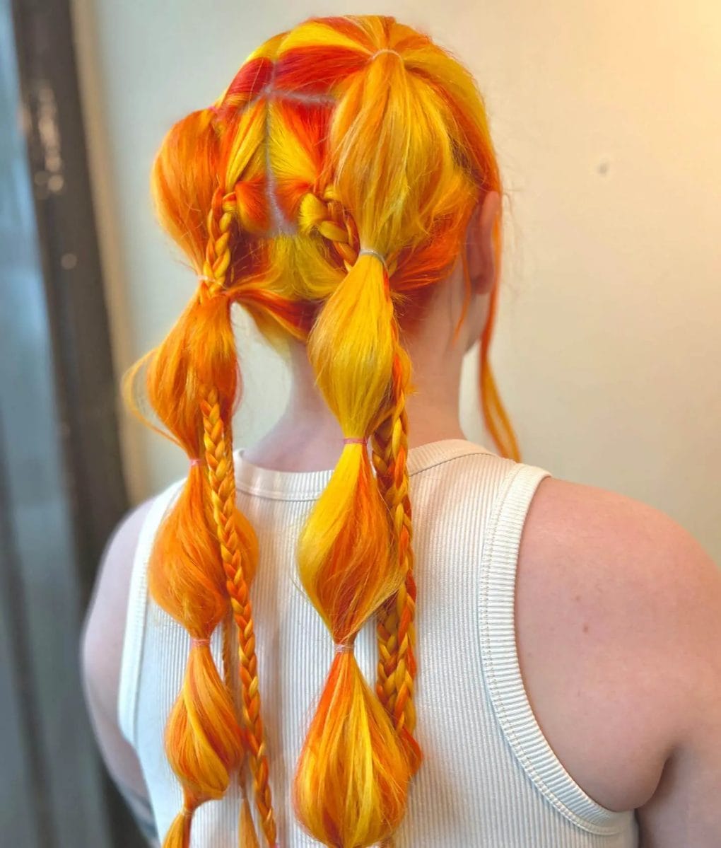 Ombré twin braids in fiery shades of orange, red, and yellow, ending in whimsical tassels for a festival look.
