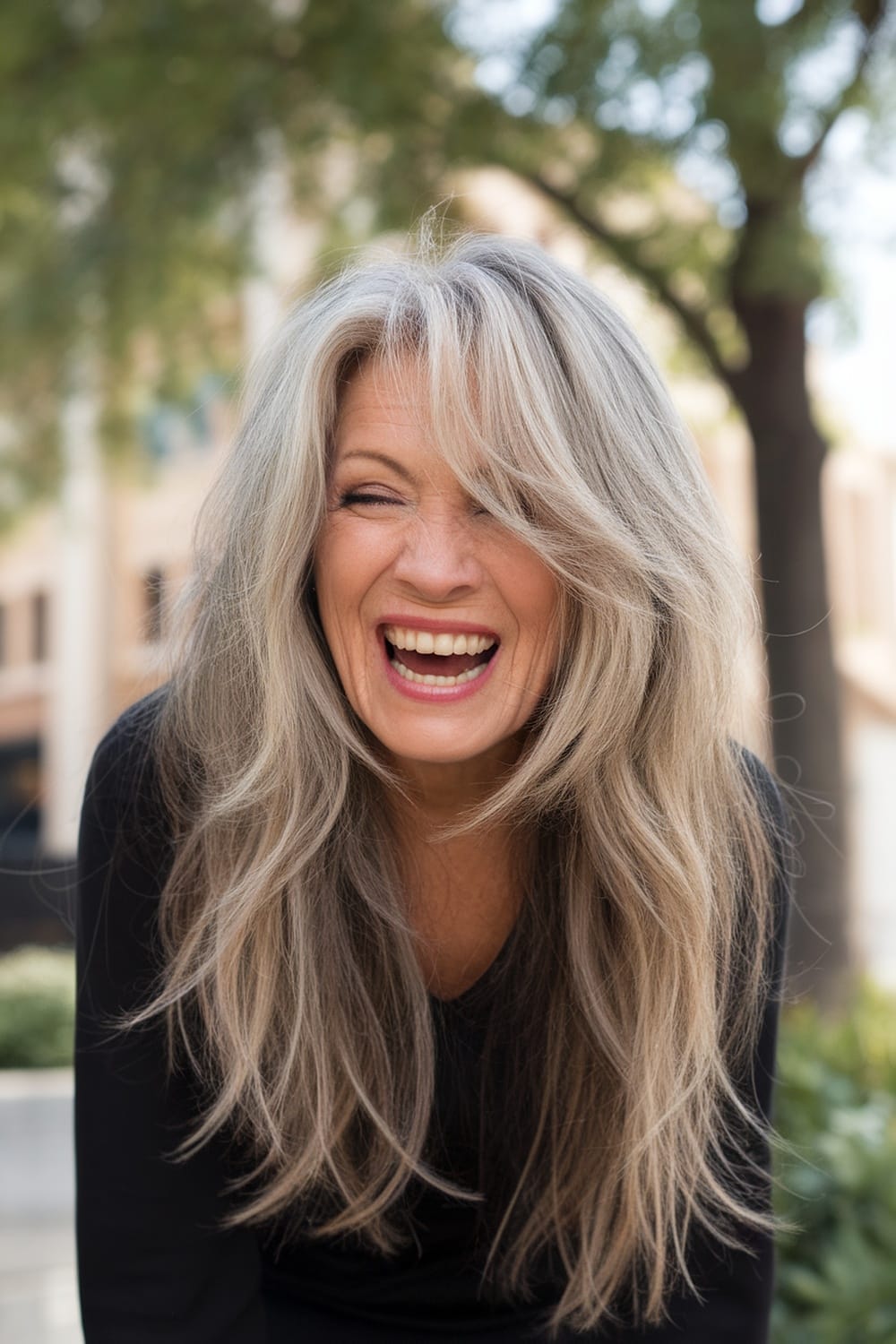 A woman with long, layered hair laughing outdoors.