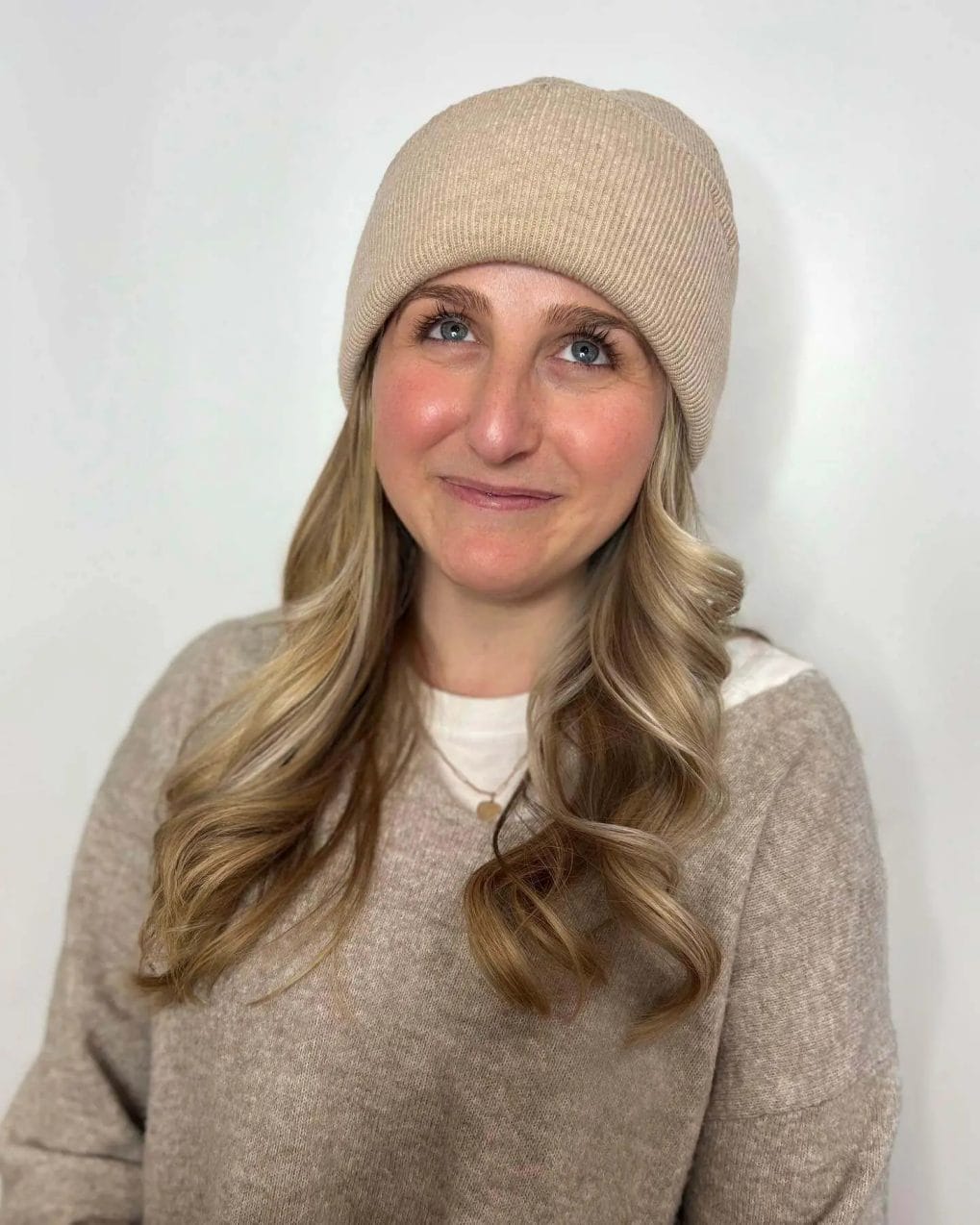 Soft bouncy curls with blonde highlights under a neutral-toned beanie.