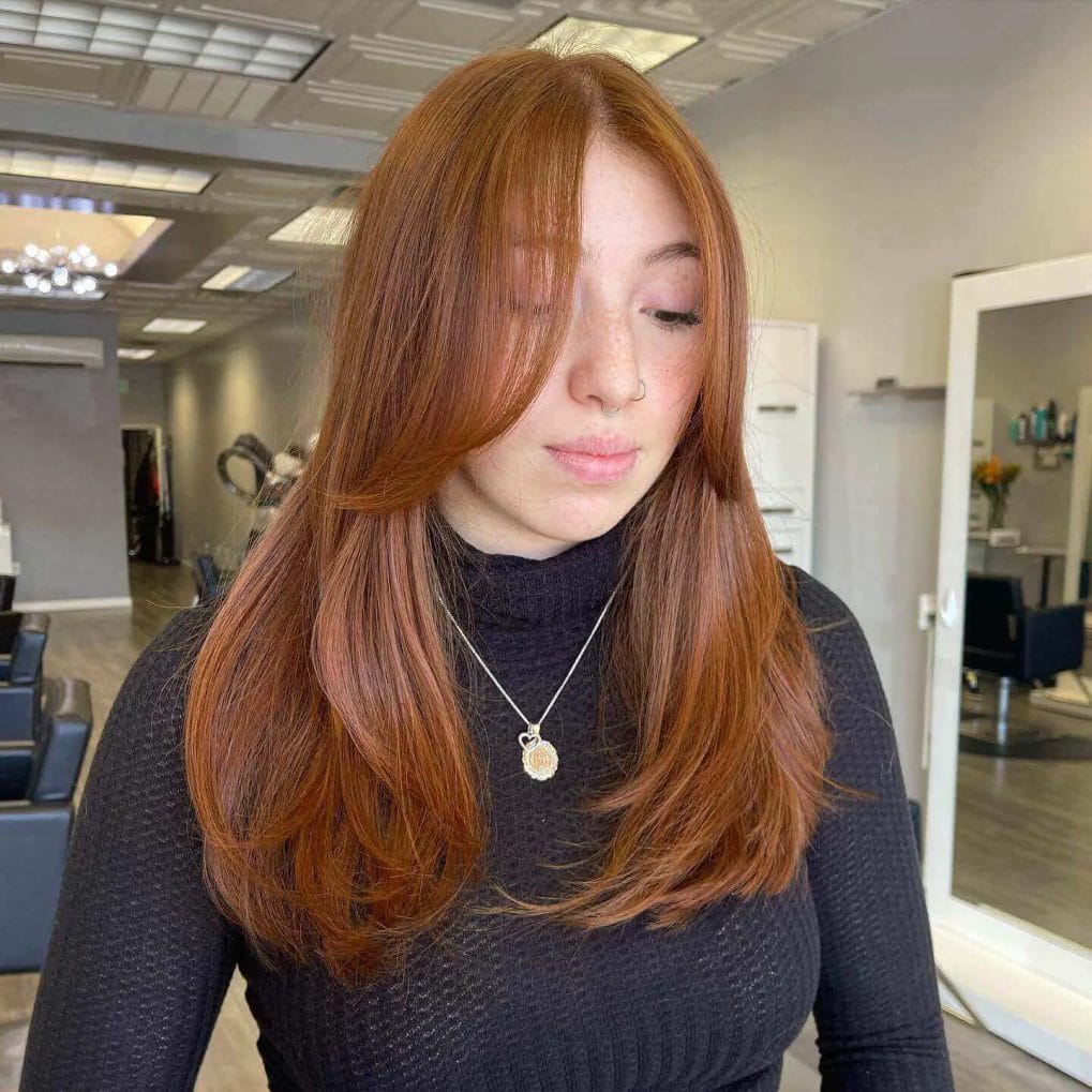Warm ginger medium haircut with feathered ends and full, straight-across bangs.
