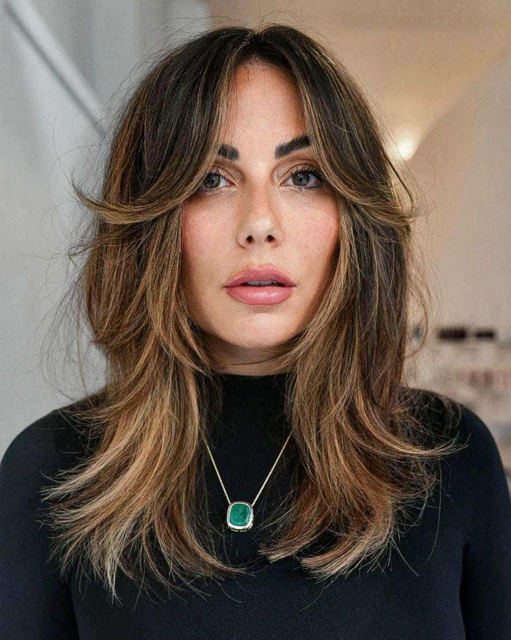 Layered medium brunette hair with soft golden highlights and sweeping curtain fringe.