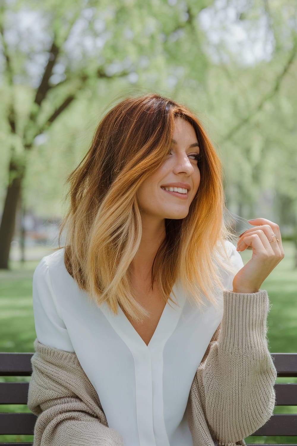 A woman with golden brown balayage hair, smiling while sitting outdoors