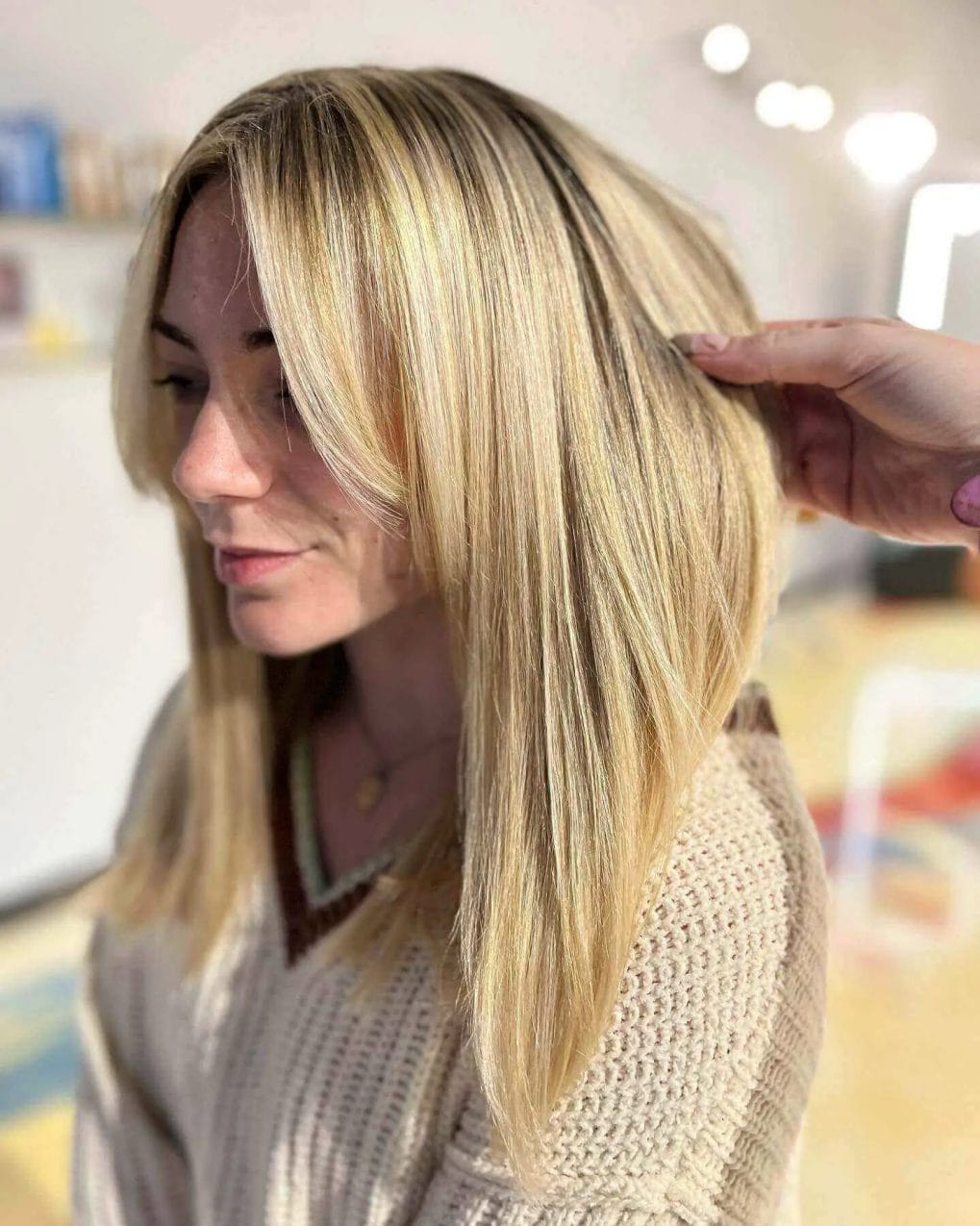 Honeyed blonde highlights in a sleek, straight medium hairstyle without bangs.