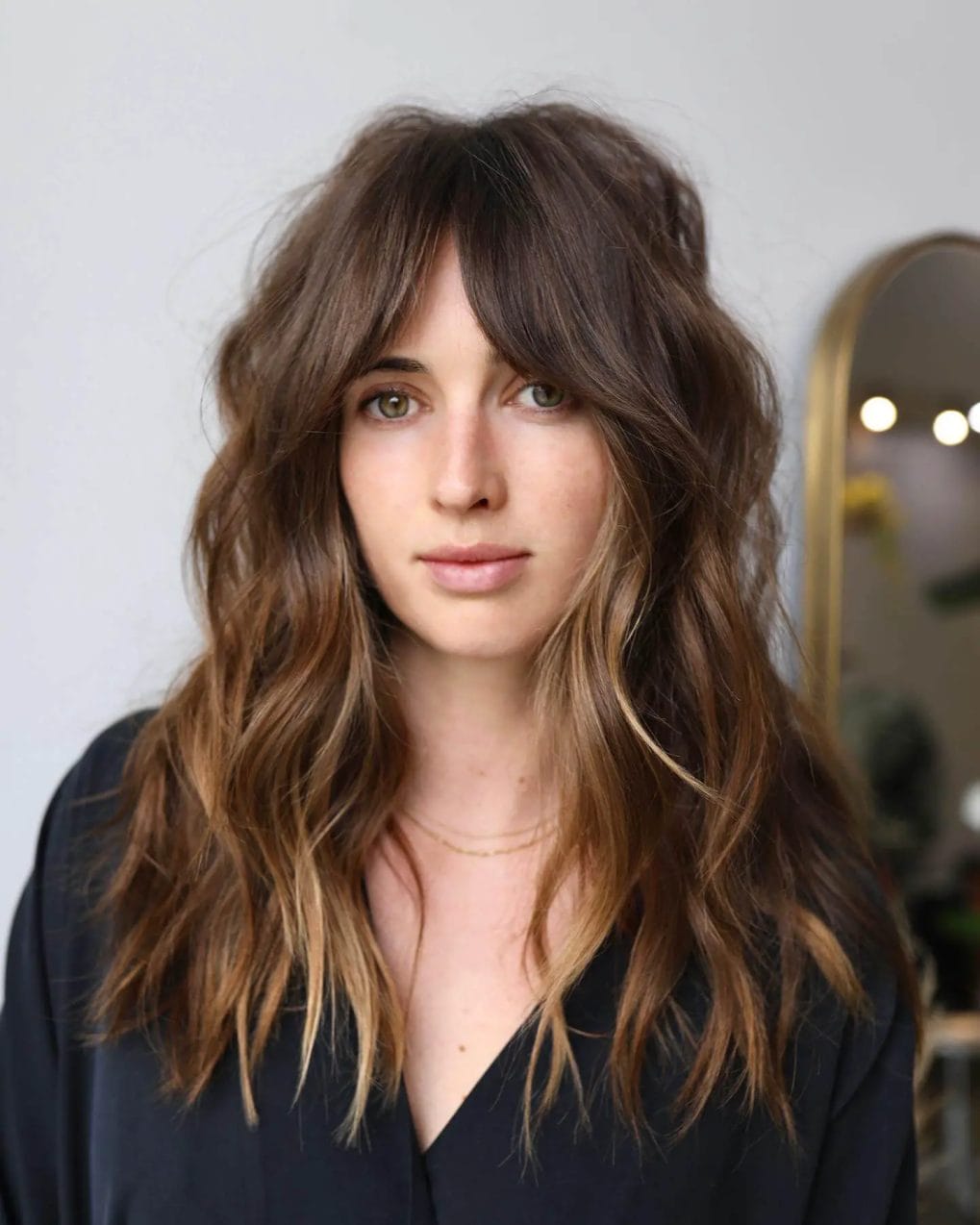 Effortlessly chic medium tousled hair with honeyed sun-kissed balayage and feathery curtain bangs.
