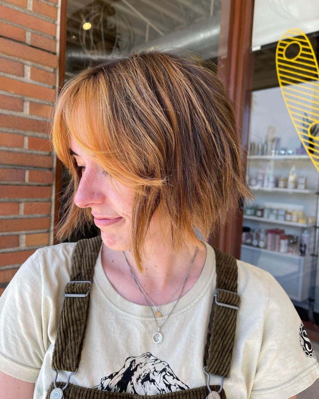 Layered honey and caramel bob with airy, feathered curtain bangs.