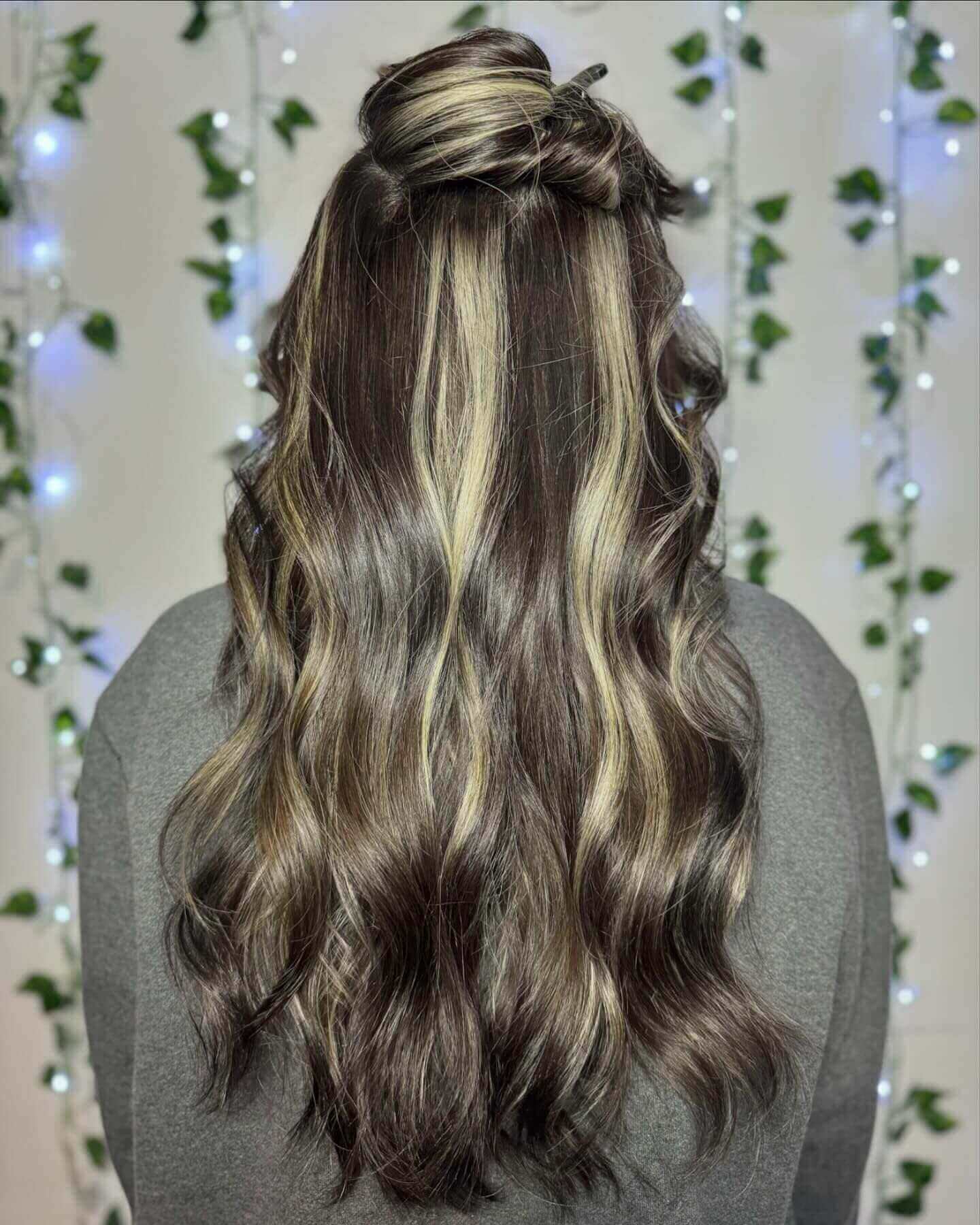 Long wavy hair with blonde and brown chunky highlights in a half-up bun