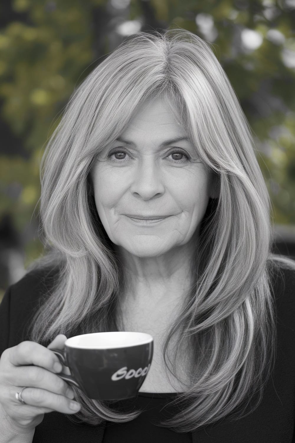 A woman with long hair and face-framing layers holding a cup, showcasing a stylish and elegant look.