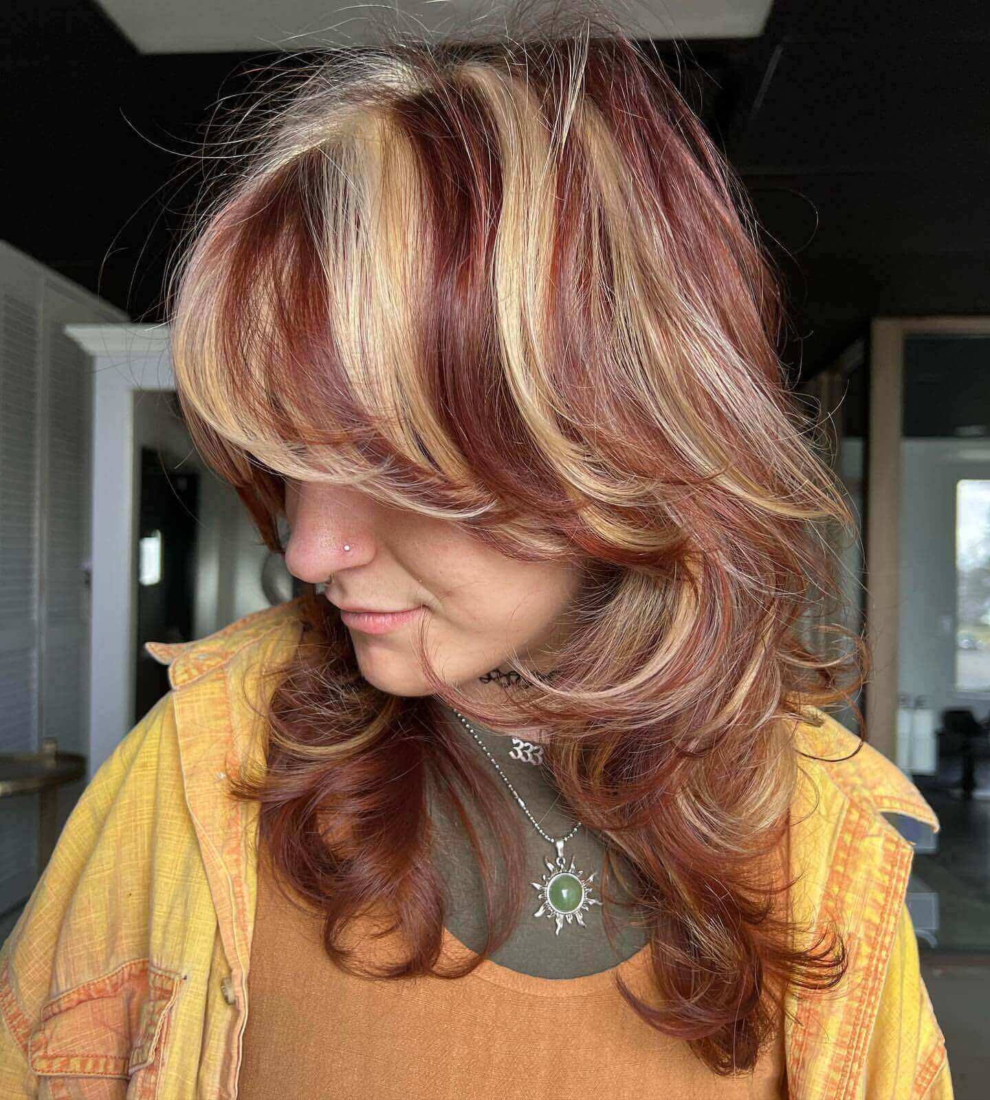 Medium layered hair with blonde and red chunky highlights and curtain bangs