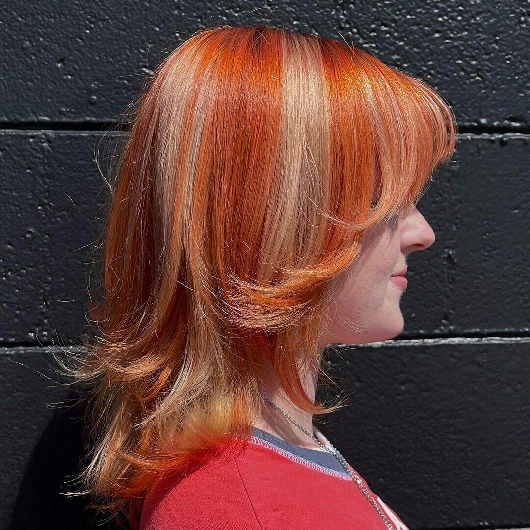Medium layered hair with orange and blonde chunky highlights and curtain bangs