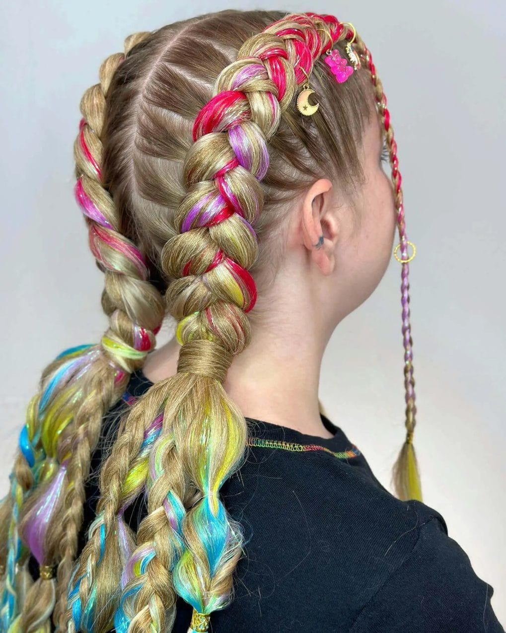 Thick Dutch braids with metallic pink and holographic strands, adorned with charms for a whimsical festival look.