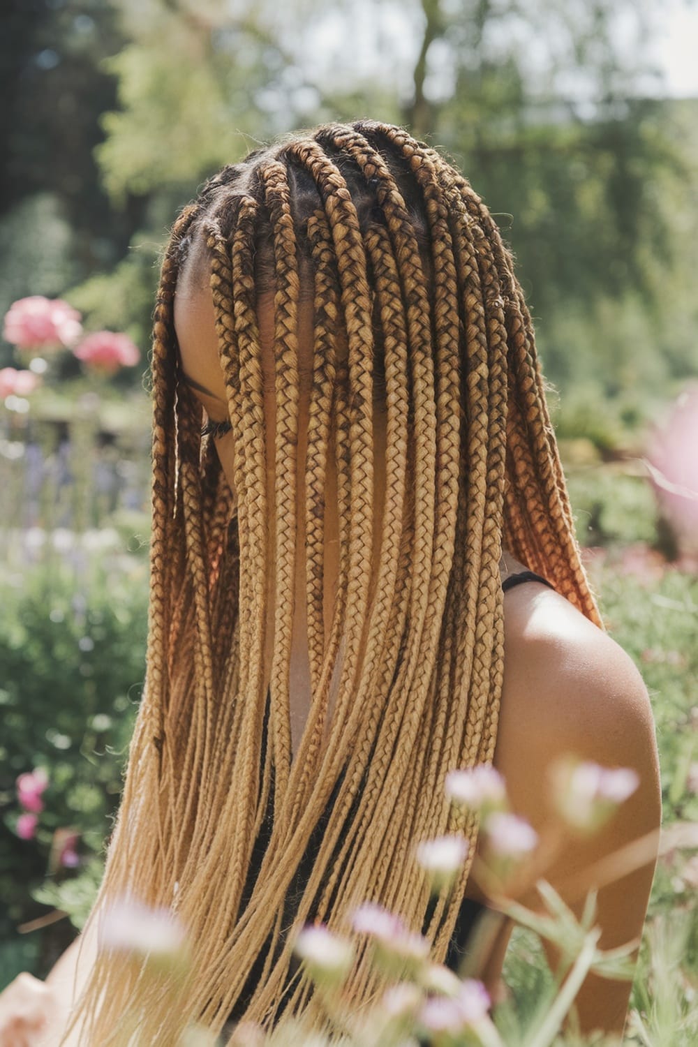 A person with micro braids featuring an ombre effect, surrounded by flowers in a garden.