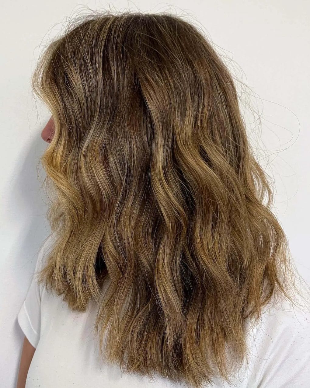 Mid-length cut with warm honey tones and soft waves on hair.