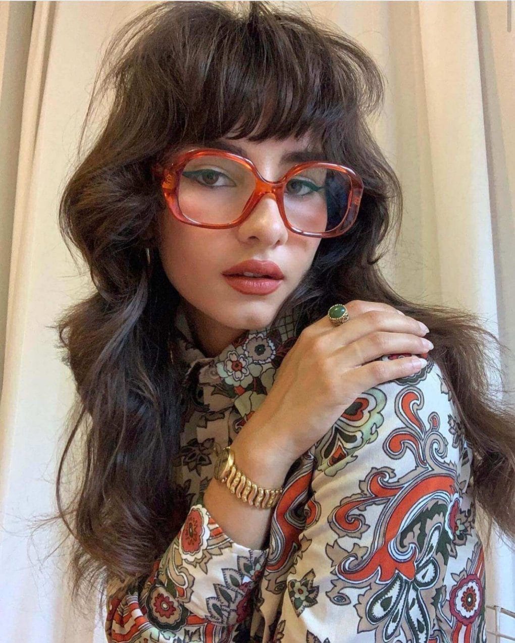 Bohemian mocha waves with full bangs and tangerine glasses.