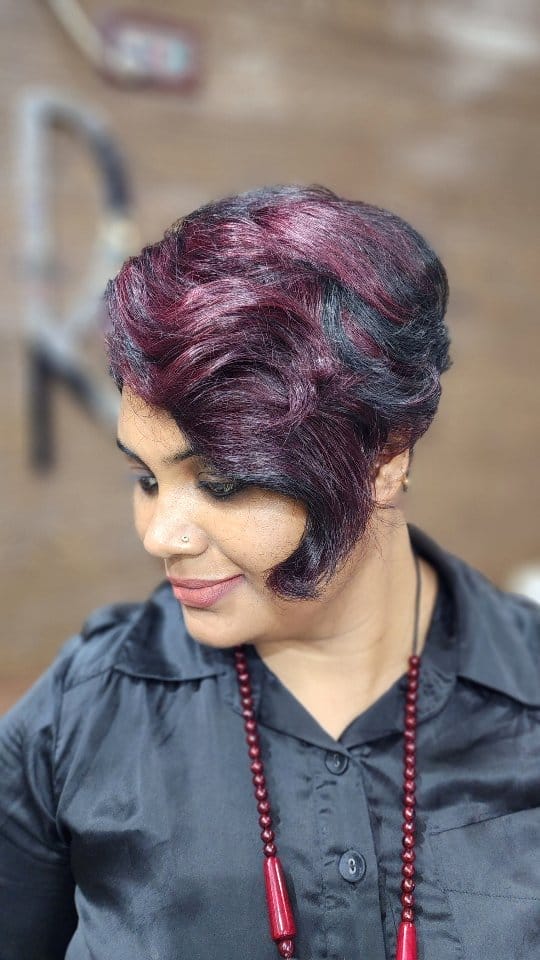 Deep burgundy voluminous pixie cut with a long swooping bang 