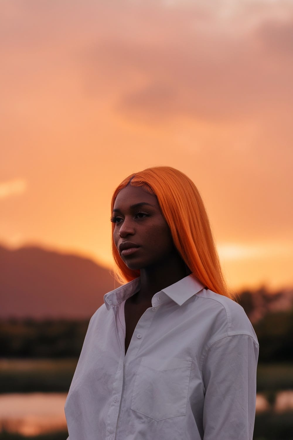 A woman with orange hair standing against a sunset backdrop