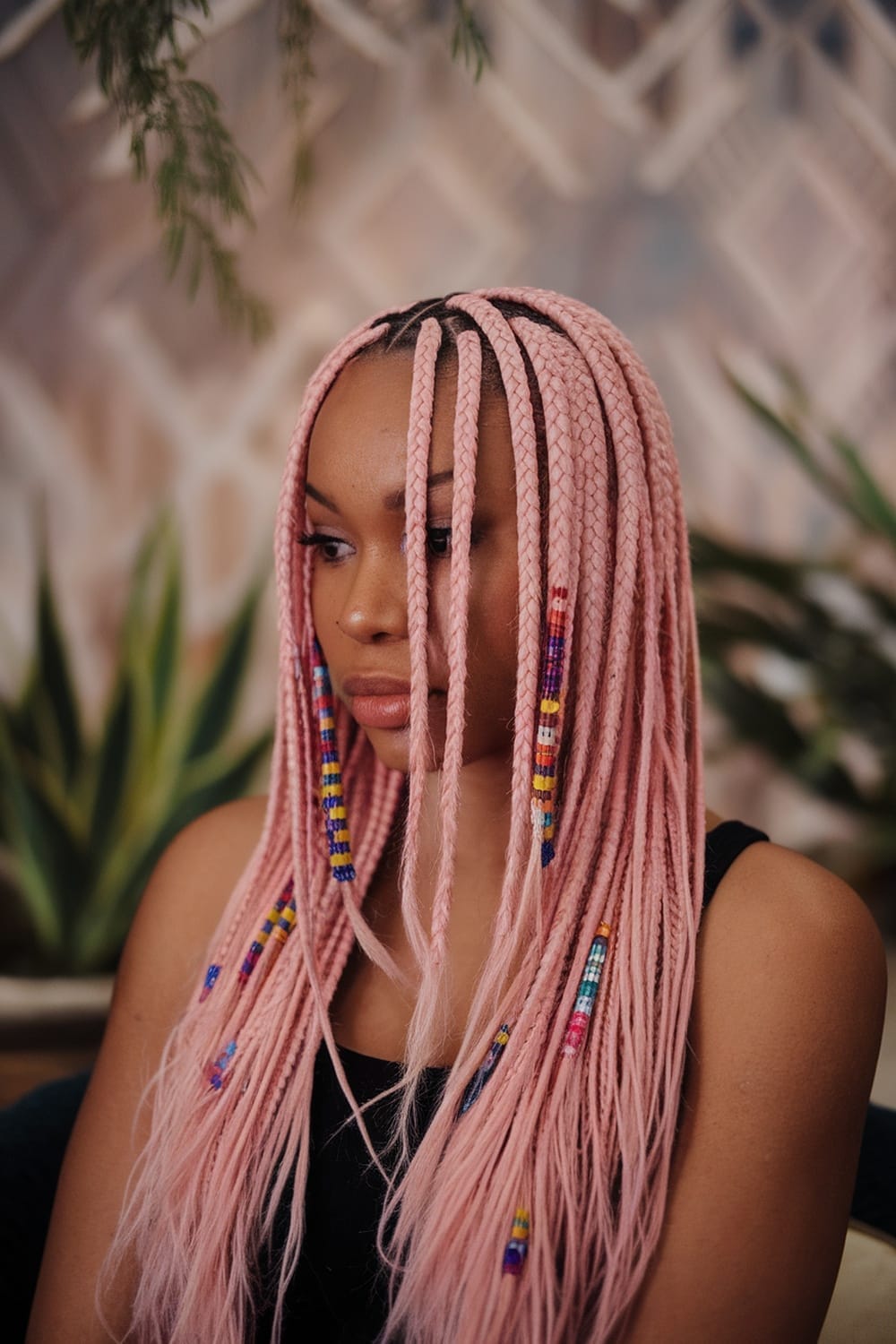 A woman with pastel pink braids adorned with colorful beads, showcasing a trendy hairstyle.