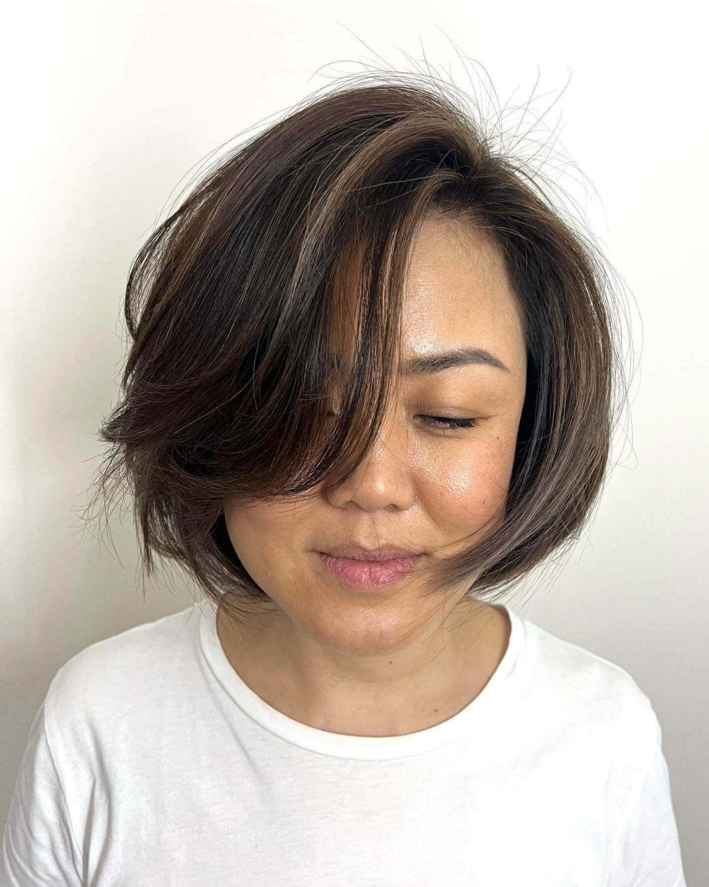 A layered bob with pearl brown highlights and feathery side-swept styling.