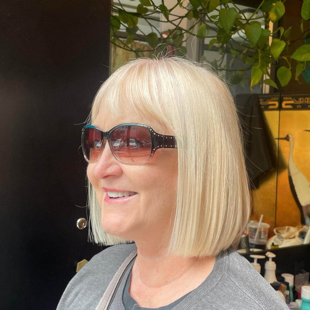 Classic bob above the shoulders in platinum blonde with straight-across bangs.