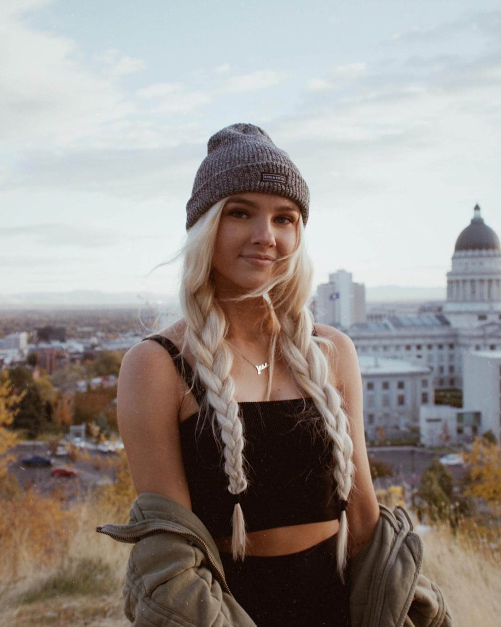 Bright platinum blonde fishtail braids under a textured slate grey beanie.