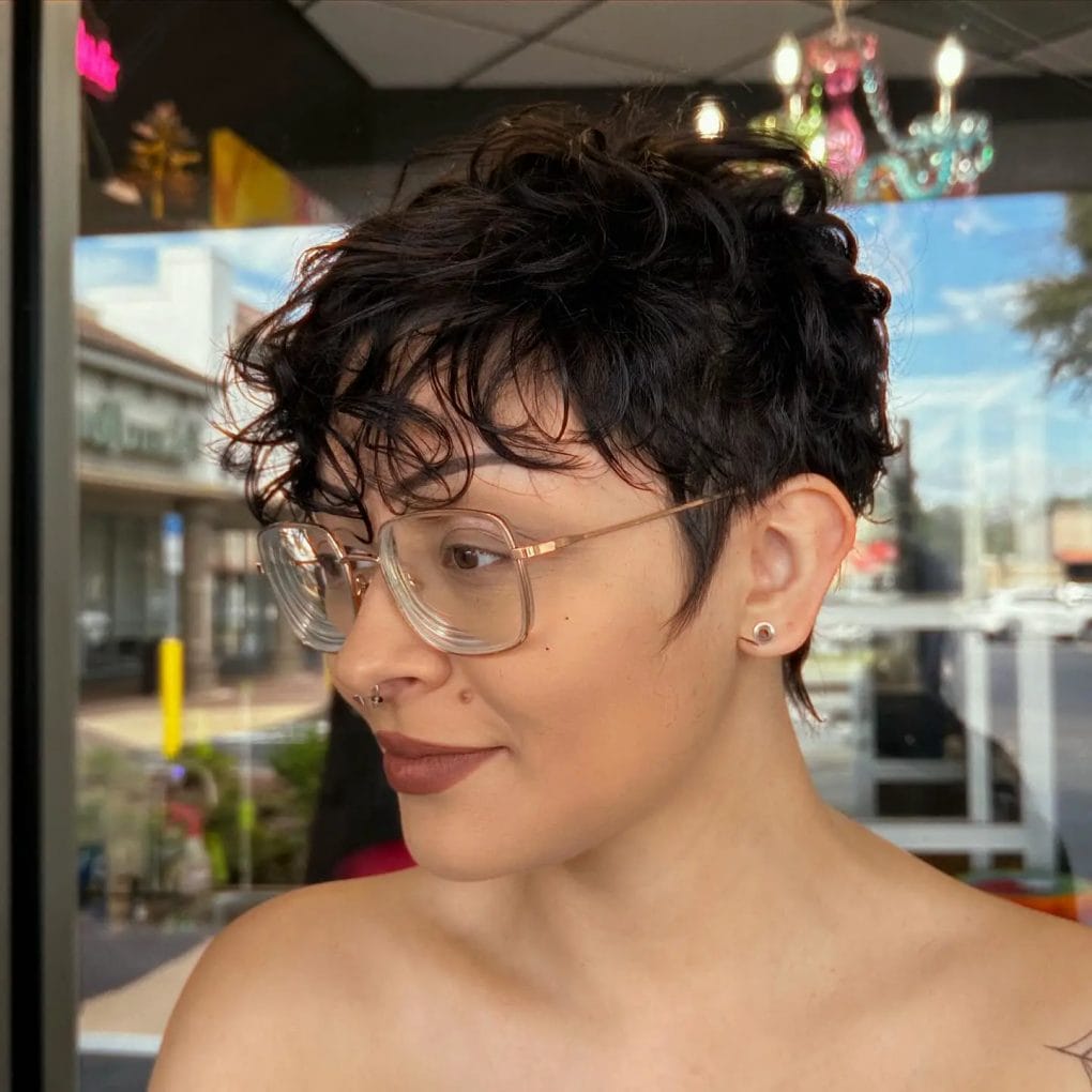 Voluminous curly pixie with whimsical side-swept bangs and circular glasses