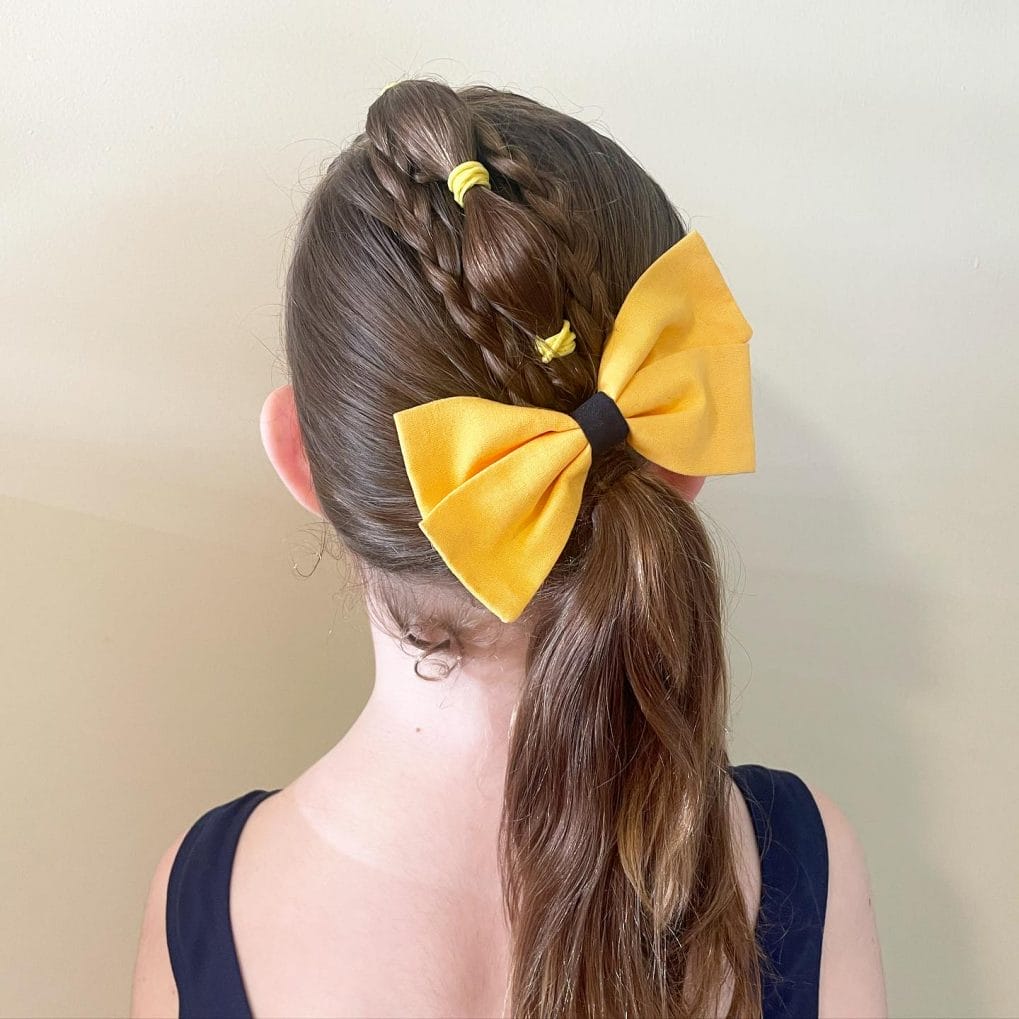Half-up hairstyle with a large bright yellow bow, combining playfulness with practicality for gymnastics