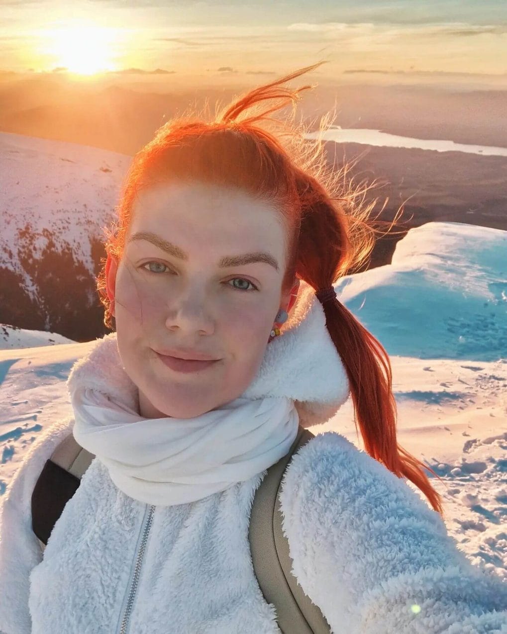 Adventurous hiker with bold red bubble ponytail against snowy landscape