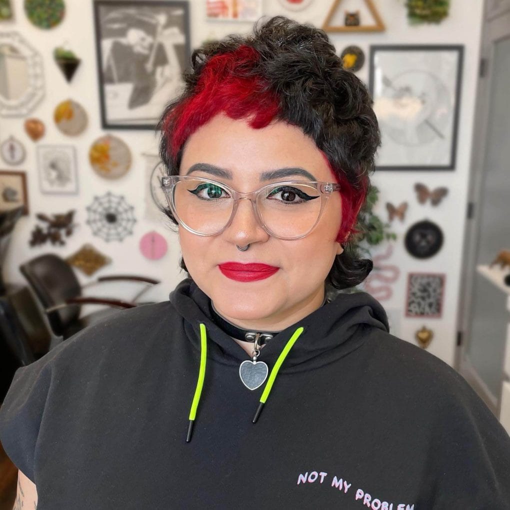 Black wavy pixie mullet with bold red bangs and sideburns.