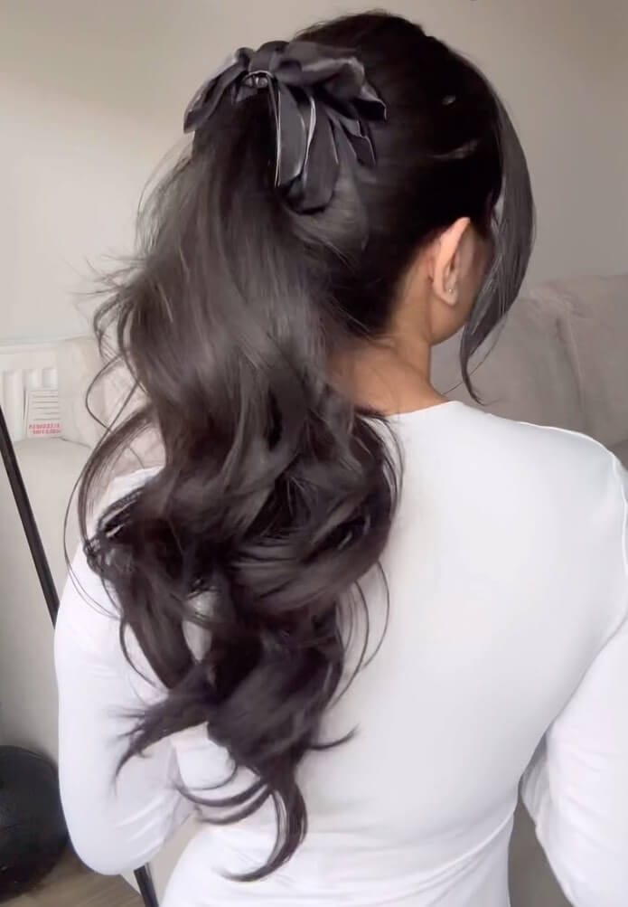 Elevated ponytail with sleek base, curls, and a satin bow for a sophisticated birthday style.
