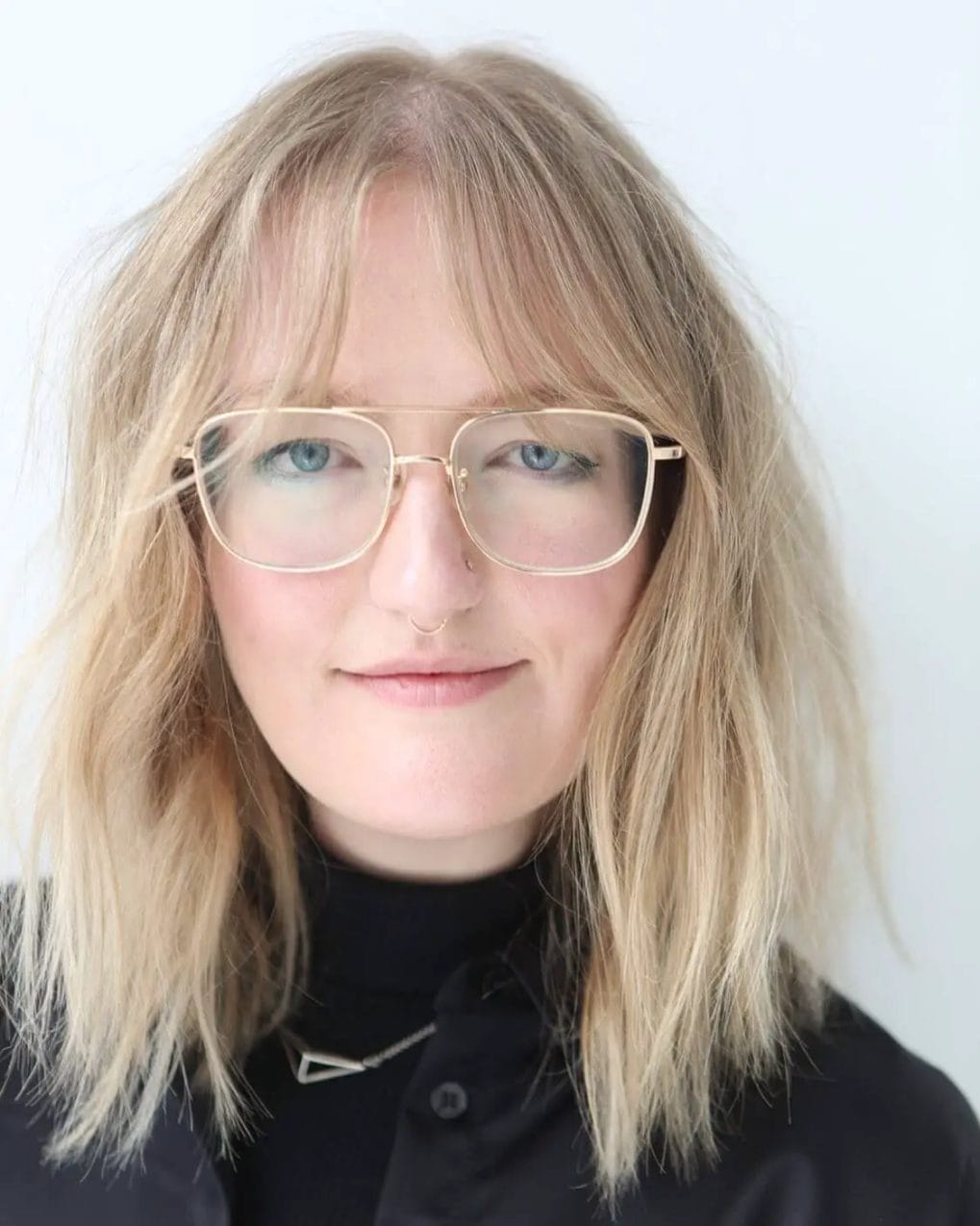 Sandy blonde tousled bob with light bangs and gold-rimmed glasses.