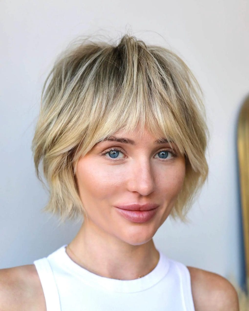 Short, choppy bob with dark roots, blonde highlights, and feathered curtain bangs.
