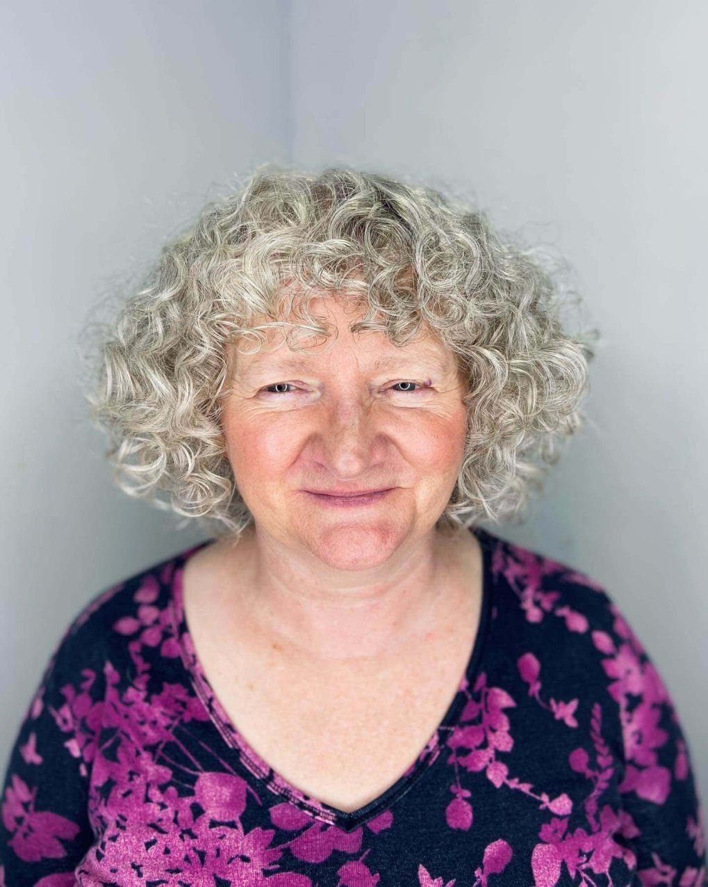 Short curly bob with ash blonde ringlets and soft, wispy bangs covering the forehead.