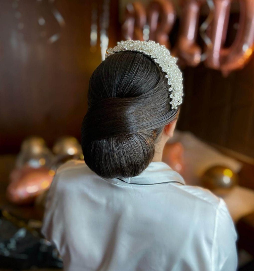 Sleek glossy bun with a pearl-embellished headband.
