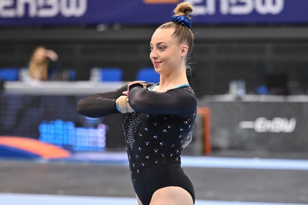 Neat high bun secured with a blue scrunchie, matching the outfit for a cohesive gymnastic look
