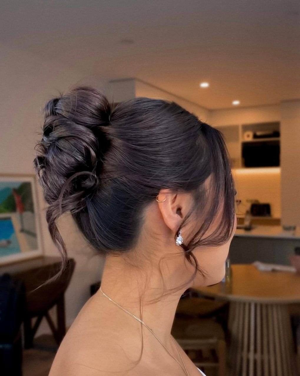 High bun with romantic tendrils in dark hair.