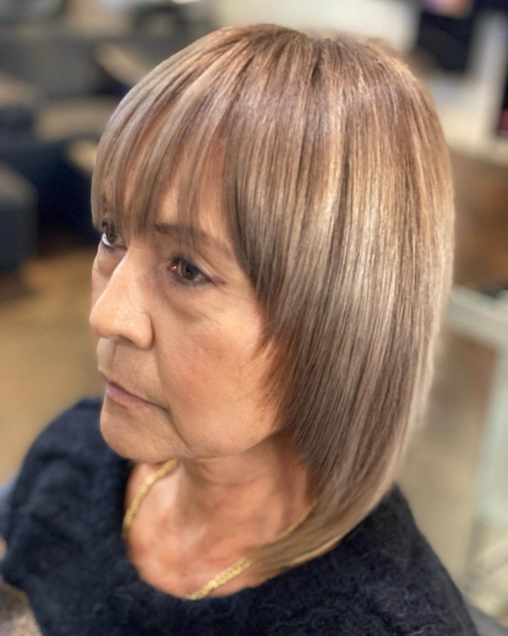 Sleek layered bob just above shoulders, straight bangs, and honey highlights.