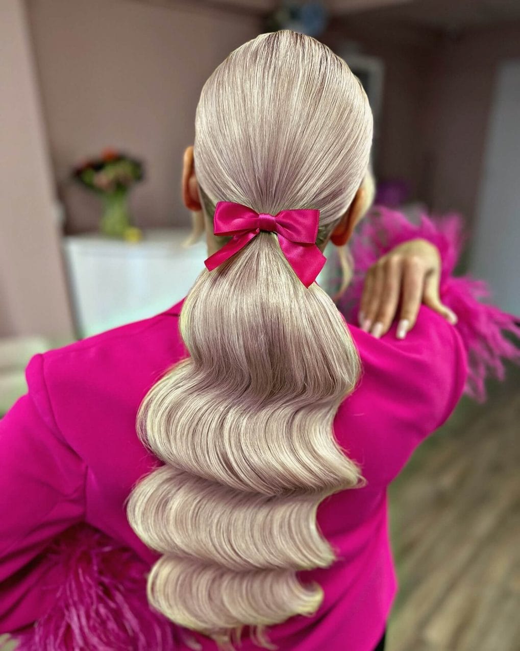 Sleek low ponytail with ice-blonde waves and pink bow