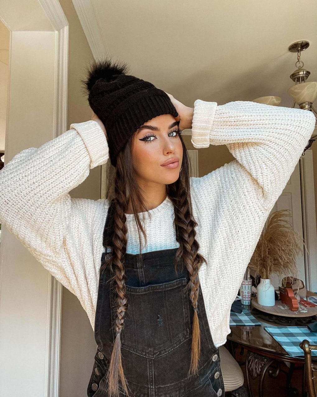 Neat chestnut-brown plaits under a black beanie with a fur pompom.