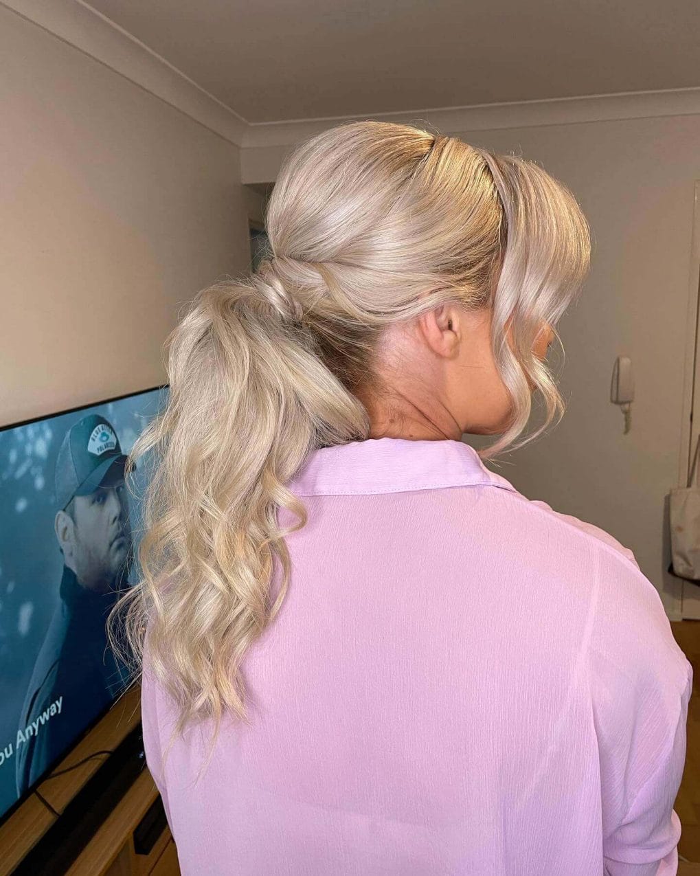 Low platinum blonde ponytail styled at the nape, with luxurious waves and modern, soft curtain bangs.