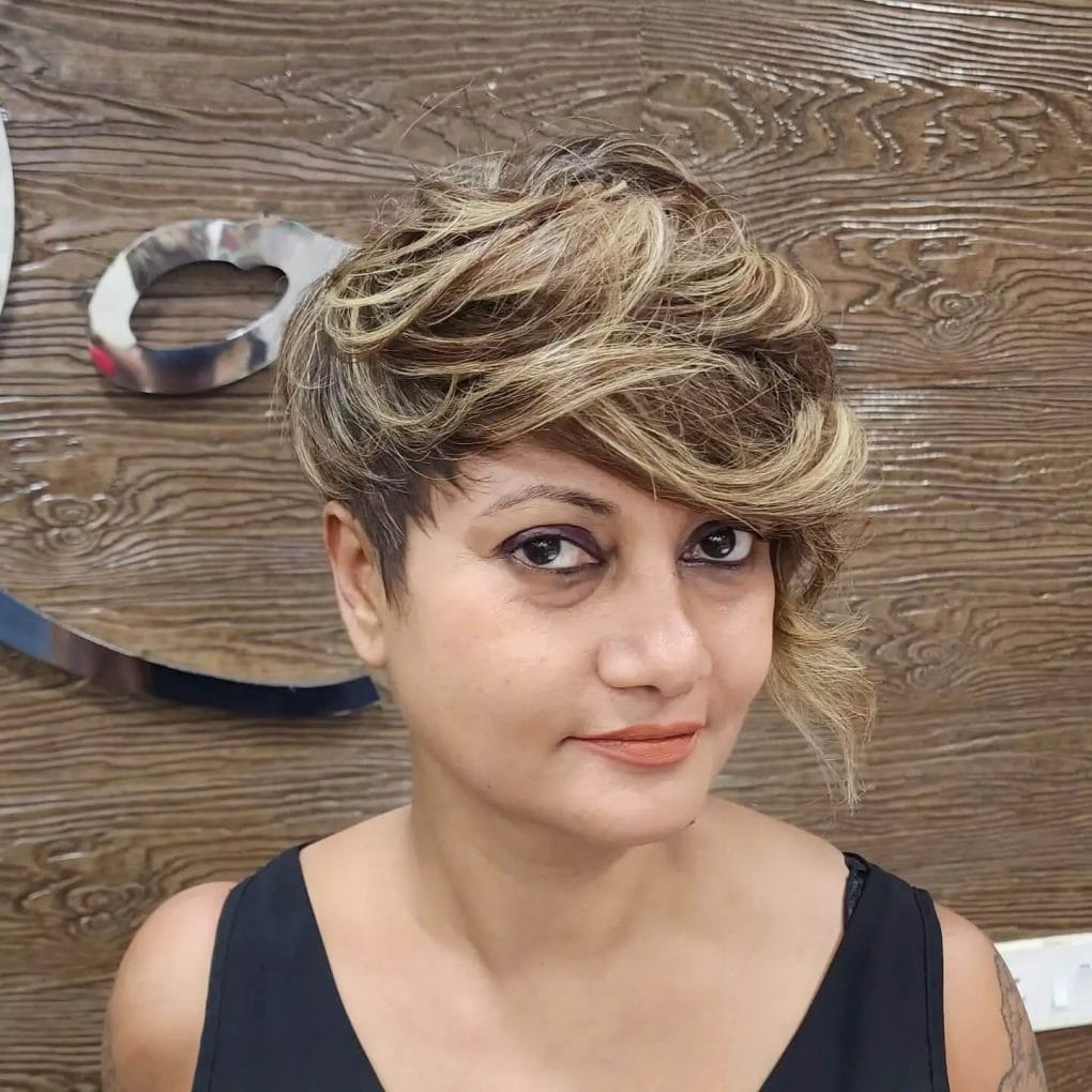 Short bixie hairstyle with golden highlights and subtle waves, accented with extended sideburns.
