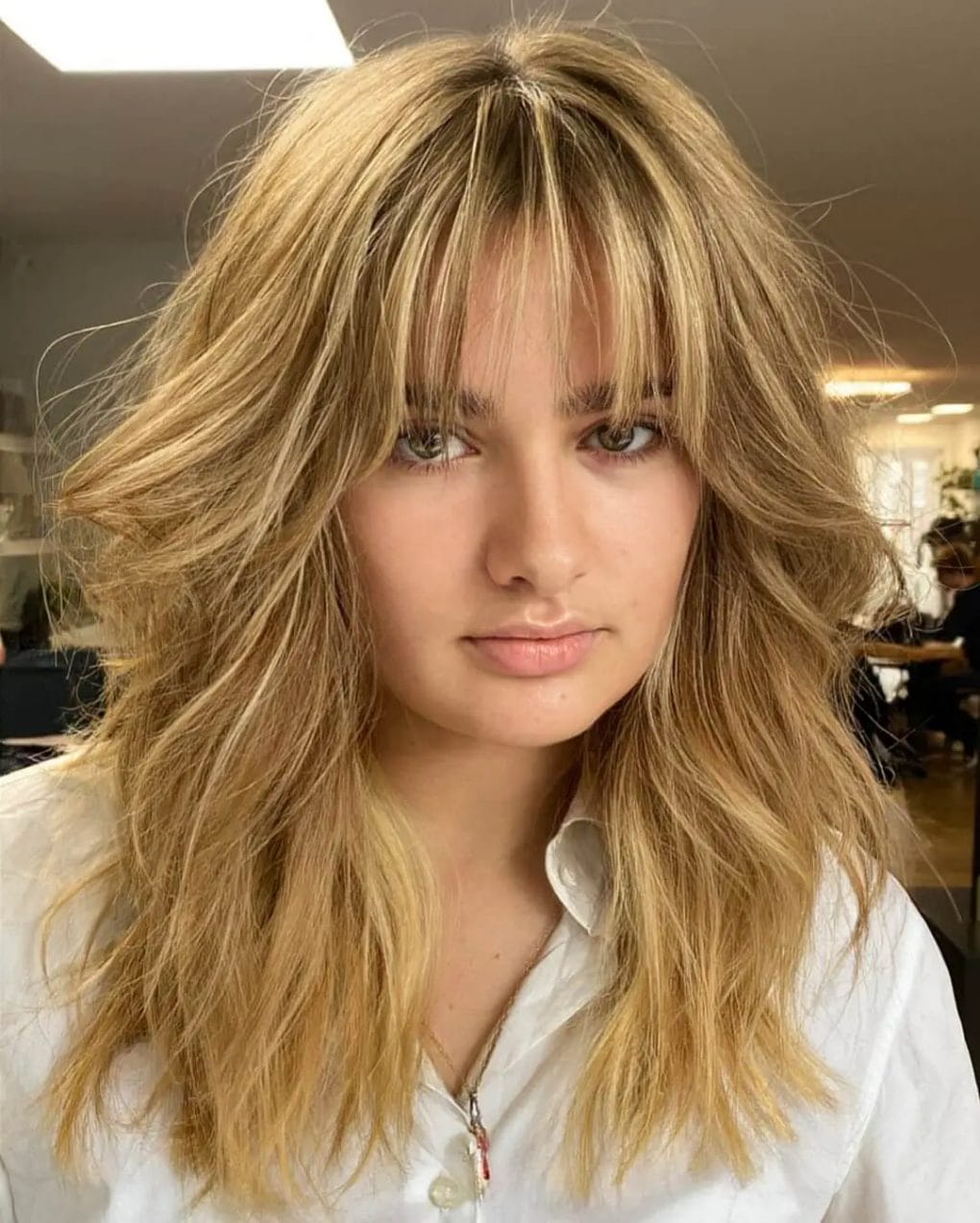 Tousled shaggy layers with soft Bardot bangs in a mix of blonde hues, perfect for a bohemian-inspired carefree look.