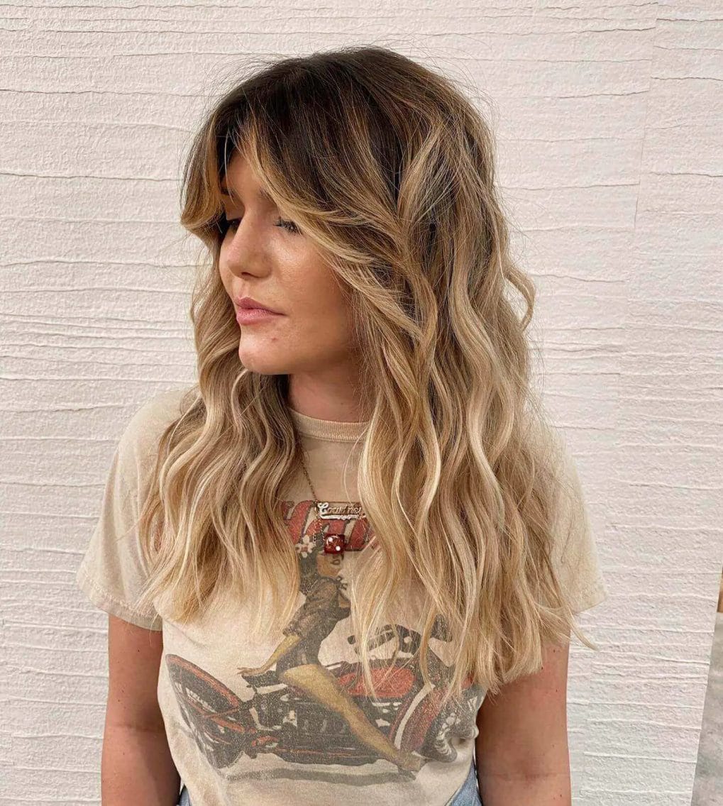 Sun-kissed balayage with bouncy curls and subtle curtain bangs.