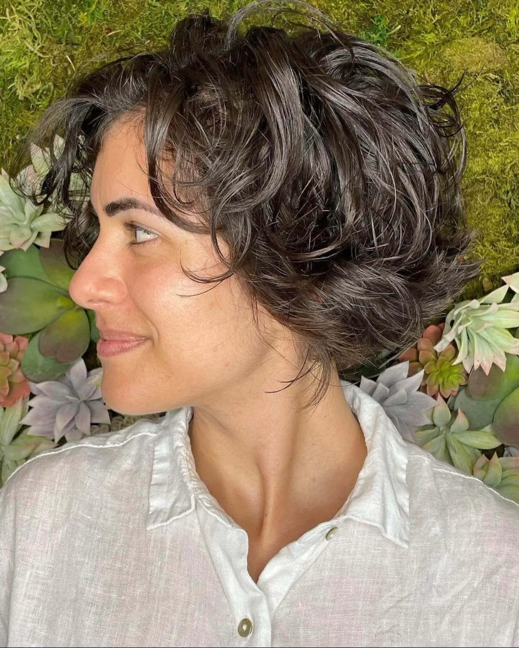 Vibrant short bixie with textured curls in glossy dark brown, ending above the neckline.