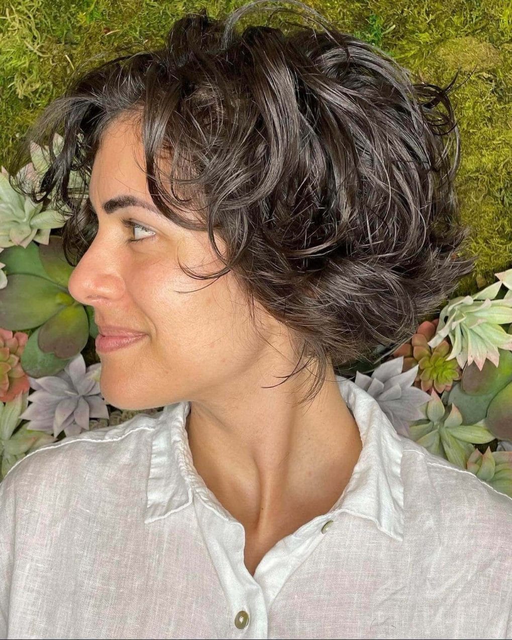 Vibrant short bixie with textured curls in glossy dark brown, ending above the neckline.