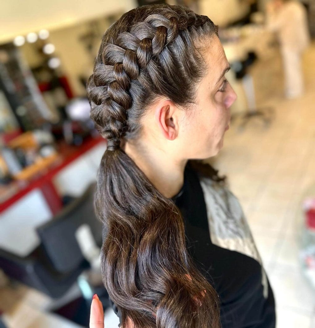 Thick braids wrap around to a low ponytail with wavy ends in deep brown