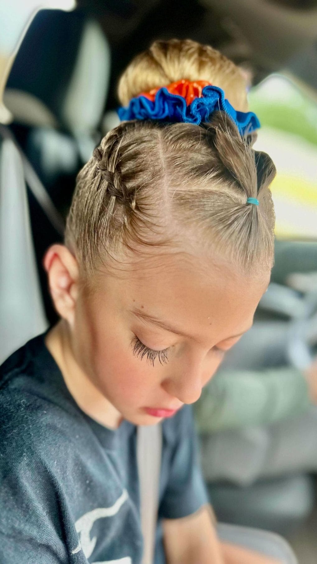 Tight braids leading to a playful bun secured with a vibrant blue and red scrunchie for a fun gymnastics style