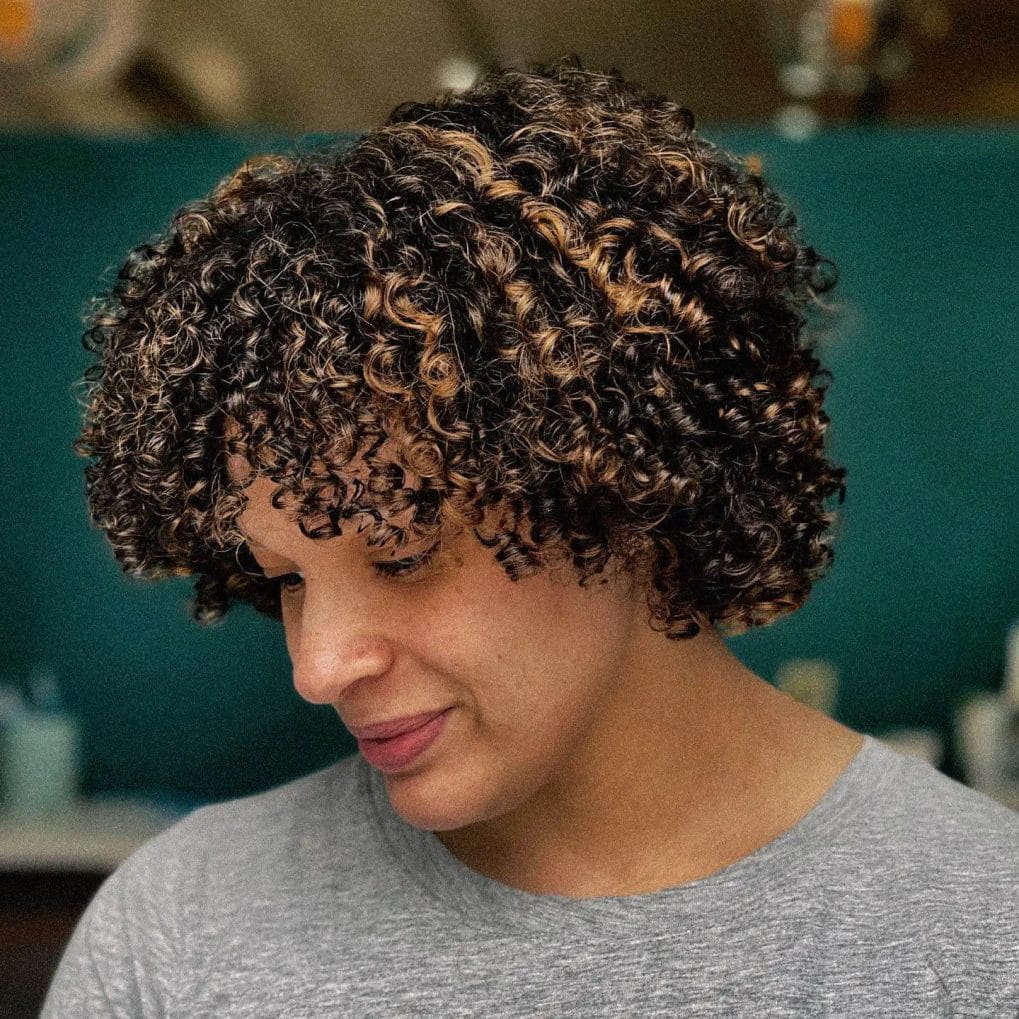 Short haircut with tightly-coiled curls and subtle highlights.